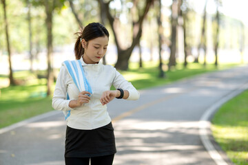 Asian adult woman athlete checking smartwatch monitoring fitness data workout progress outdoor park running trail healthy lifestyle journey health technology device sports activity