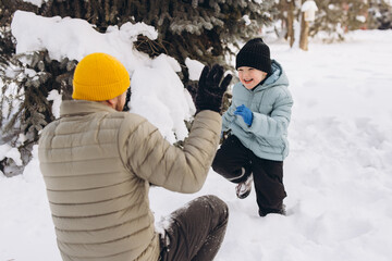 Father and son playing snowball fight in winter forest, boy laughing and having fun outdoors