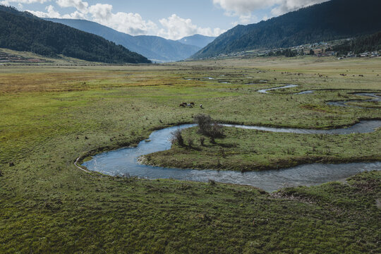 Aerial view of the meandering river cutting through the lush green valley floor, framed by distant mountains, Phobjikha Valley, Wangdue Phodrang, Bhutan.