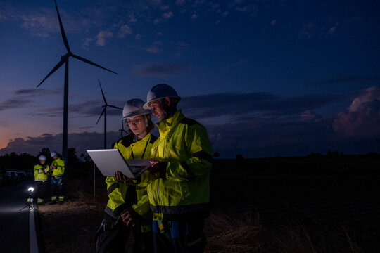 Working team checks data at wind farm during evening with wind turbines in background near highway - Powered by Adobe