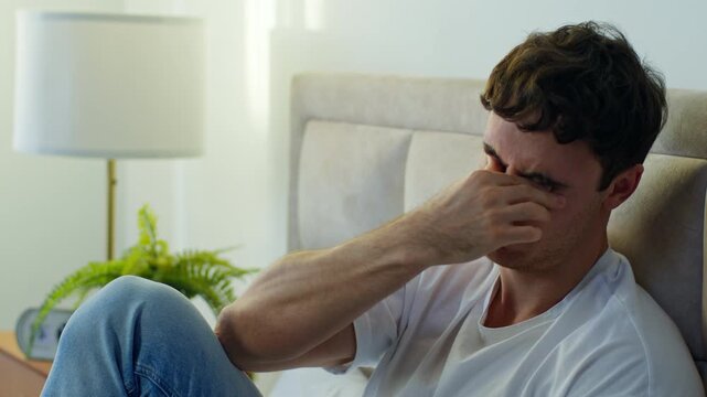 Sad suffering Caucasian young man feeling overwhelmed stressed resting bed at home bedroom thoughtful male guy touching temple fatigue pain illness headache anxiety indoors burnout concern exhaustion