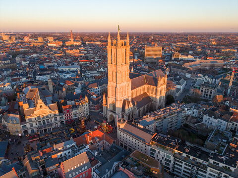 Aerial view of the imposing Saint Bavo Cathedral piercing the skyline amidst the warm glow of sunset, Ghent, Flanders, Belgium.