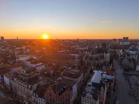 Aerial view of the sun setting behind the Saint Nicholas Church, casting a golden glow over the historic buildings, Ghent, Flanders, Belgium.