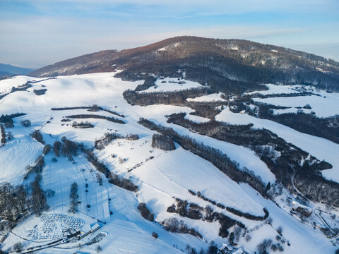 Aerial view of a landscape where a blanket of snow covers the hills and trees, creating a serene contrast against the clear sky, Viglasska Huta-Kalinka, Banska Bystrica Region, Slovakia.