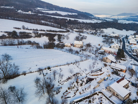 Aerial view of snow-covered fields and rooftops meet the stark outlines of trees and winding roads, Viglasska Huta-Kalinka, Banska Bystrica Region, Slovakia.