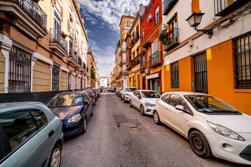 Obraz premium Narrow street in Seville with colorful residential facades with parked car, Spain. Beautiful architecture in Andalusia, Europe.