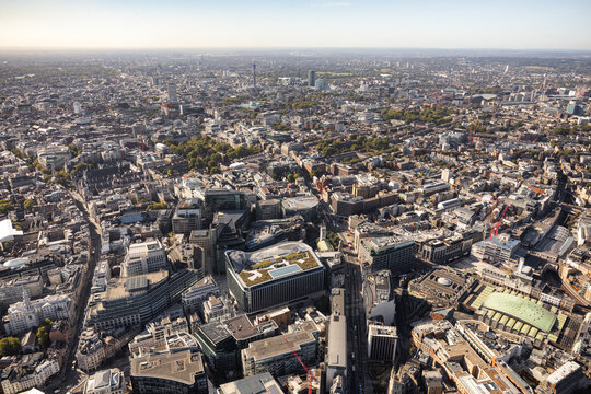Aerial view of modern buildings casting long shadows in the late afternoon sun, creating a stark contrast with the winding streets below, City of London, London, United Kingdom.