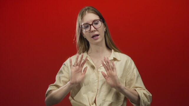Woman practicing breathing meditation with open palms gesture against vivid red studio backdrop; calmness.