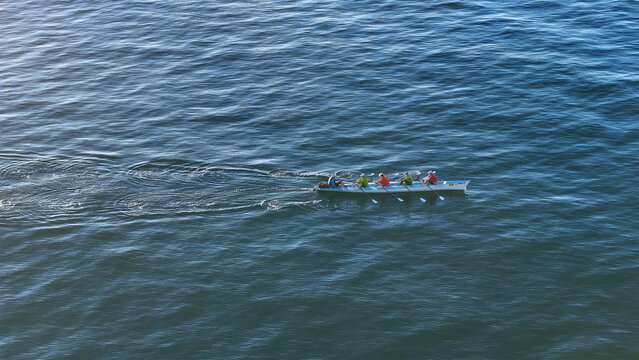 Aerial view of a rowing team slicing through the tranquil, sun-kissed waters, leaving a trail of shimmering ripples behind them, Cape Town, Western Cape, South Africa.