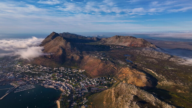 Aerial view of dramatic peaks meet the sea as clouds embrace the slopes, and a vibrant city nestles at the mountain's base, Cape Town, Western Cape, South Africa.