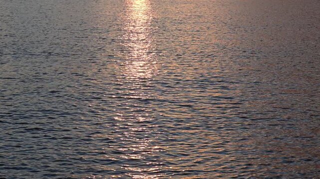 the golden sunlight shimmering across the gently rippling surface of the sea during sunset, creating a glittering path of light.