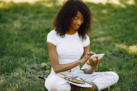 Female african student sitting on a grass and using a tablet