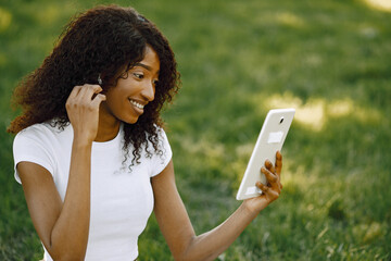 Female african student sitting on a grass and using a tablet fo a video call