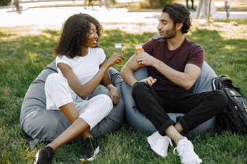 Indian boy and african girl talking sitting on the bean bag chairs in a park