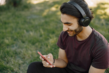Male indian student sitting on a grass and using a smatphone