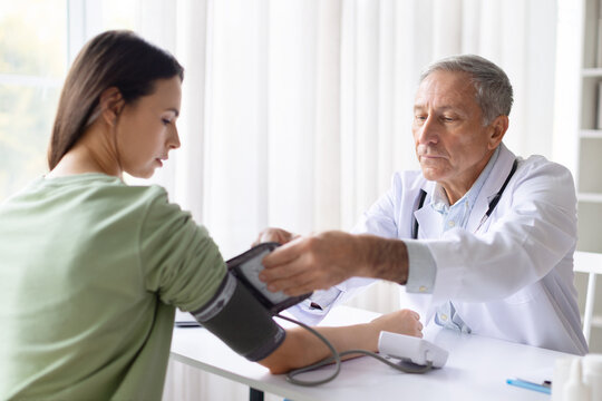 Senior male doctor measuring blood pressure of female patient using tonometer in clinic, routine health check and preventive medical examination