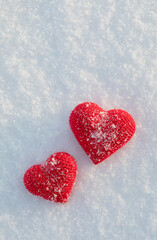 Knitted two red hearts on white snowy background in sunny winter for Valentine day greeting card.