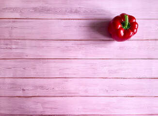 
One red bell pepper on a background of pink boards. In the upper right corner.

