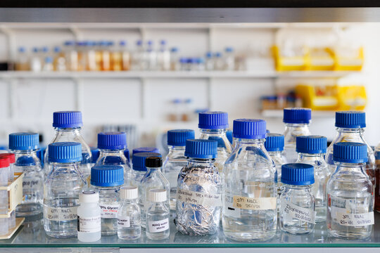 Transparent bottles with blue caps containing different chemical liquids on a shelve in a lab