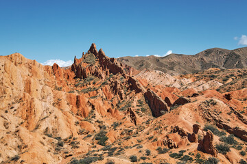 Fototapeta premium Red rock formation at Fairy Tale Canyon in Kyrgyzstan. Mountain landscape for travel and adventure concept. Outdoor desert scenery.