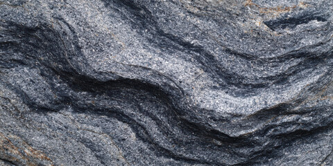 Calming close up view of dark gray rock texture. This natural stone background shows an abstract wavy pattern on its surface, beautiful example from geology