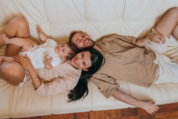 A family of three relaxively lying together on a cream-colored couch, embodying warmth, love, and togetherness in a cozy setting.