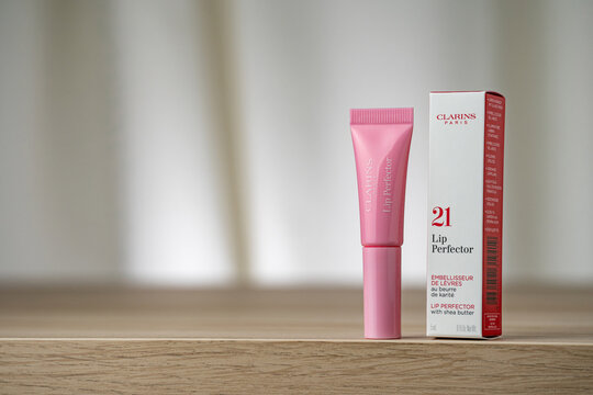 STRASBOURG, FRANCE - JANUARY 15, 2026 : A still life photographe of Clarins Lip Perfector lip gloss tube packaging box. The product is displayed on a wooden surface, cream drapes background in soft