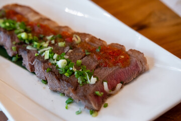 Japanese sliced medium rare steak served on plate, topped with sliced spring onion and sauce