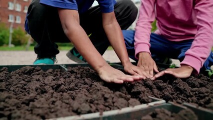 Children joyfully plant seedlings in a community garden. Captured from a low angle, the video emphasizes teamwork and environmental care.