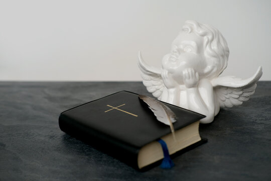 old black book, family bible in dark cover, white ceramic figurine of angel with wings, goose feather, concept of intermediary between God and world, eternal Christian values, unity of people in faith