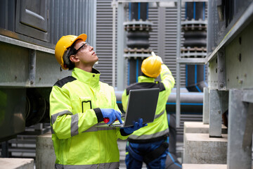 Engineers at work in a technological facility, analyzing with their laptop computer. Focused on the data, the workers are involved in technical operations and maintenance