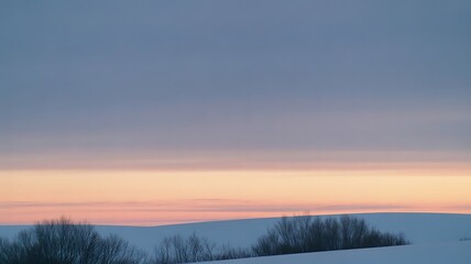 Snow covered rolling hills meet a pale horizon displaying soft pastel colors during a winter twilight.