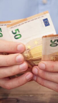 Vertical close-up of male hands counting euro banknotes. Man in blue shirt counting money, European currency. Financial background for salary, savings or budget planning. Investor counting money.