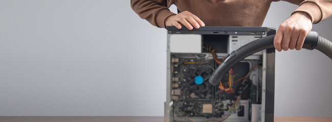 Man cleans a computer case with a vacuum cleaner.