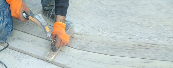Carpenter with hammer hitting nail on wooden plank.