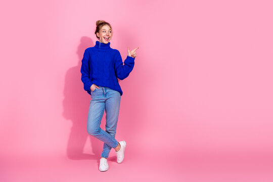Young woman in blue knit sweater smiles and points against pink background in a casual stylish lifestyle photo