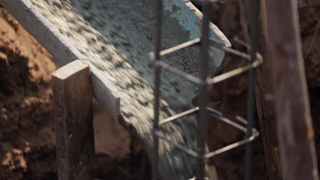 Steel rebar cage receiving fresh concrete mix from construction truck chute during footing work at a foundation job site.