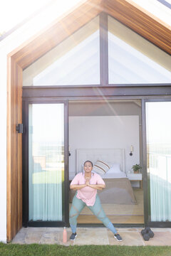 Mid adult African American woman doing squat on patio by bedroom in athletic wear, dumbbells close