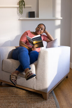 African American woman reclining and reading ENDLESS SUNSETS paperback in armchair in living room