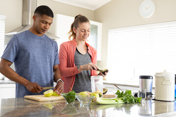 Couple slicing apples with kitchen knife, scooping avocado into blender jar in modern kitchen