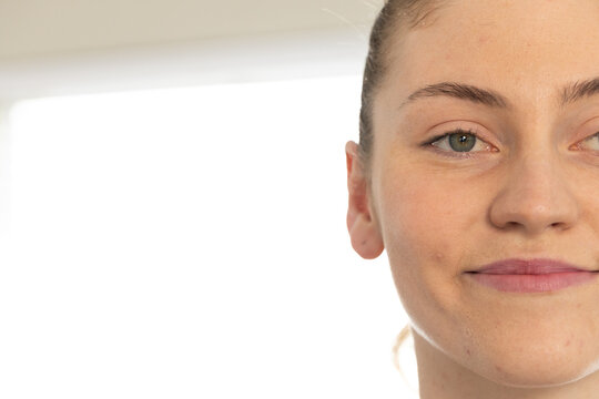 Woman facing camera, subtly smiling, hair pulled back near bright window, copy space