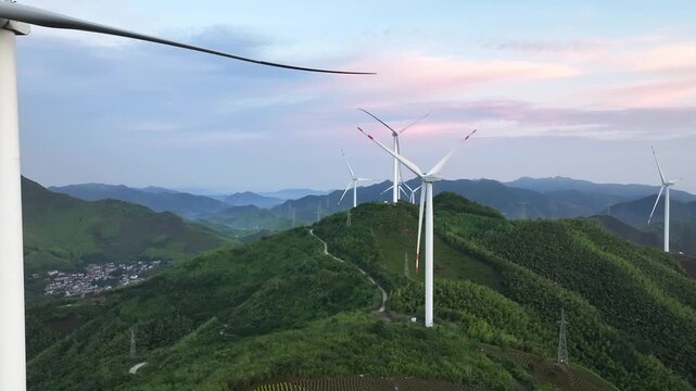 Wind turbines rotating on mountain ridges during sunset with green hills and natural landscape