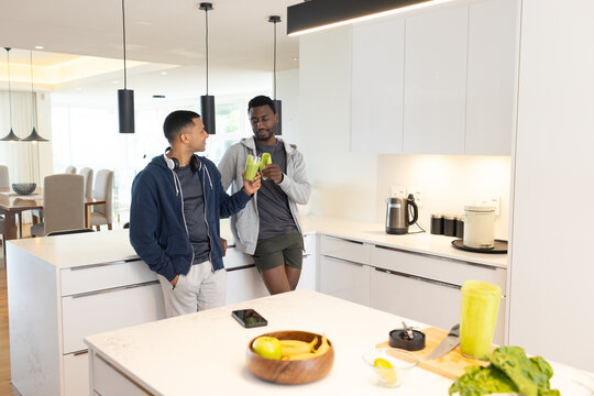 African American man and male friend leaning at kitchen island, holding green smoothie near phone