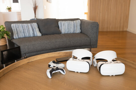Two white VR headsets and controllers are resting on round wooden coffee table in living room