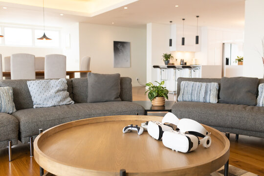 Round wooden coffee table is holding two white VR headsets and wireless controller in living room
