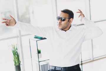 Dynamic young businessman in a white shirt and sunglasses performs energetic pose in a modern office loft