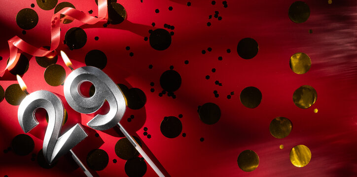 Concept of celebrating birthday and anniversary. Number 29 twenty-nine silver celebration birthday candle on festive red background with large golden confetti. Twenty-nine years birthday. - Powered by Adobe