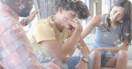 Comforting friends placing hand on man in yellow tee leaning on home sofa, wristwatch prism overlay