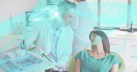 Reclining patient in yellow seat receiving exam in clinic, in teal blouse, dentist holding model