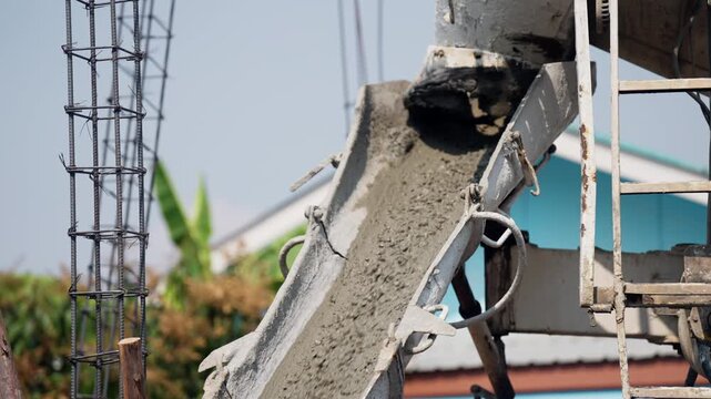 Concrete truck chute delivering wet cement into reinforced formwork at a building site, foundation construction in progress.